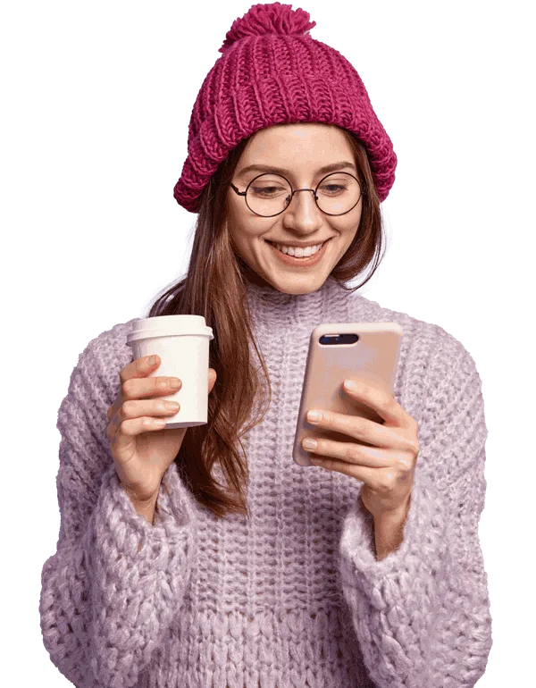 Mujer con gorro de lana y taza de café mirando su teléfono móvil